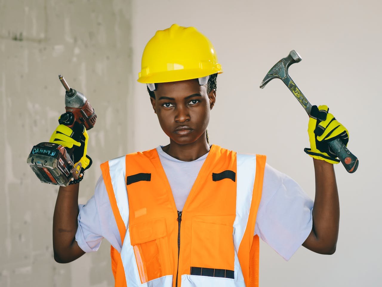 A focused worker wearing protective gear holding a drill and hammer indoors.